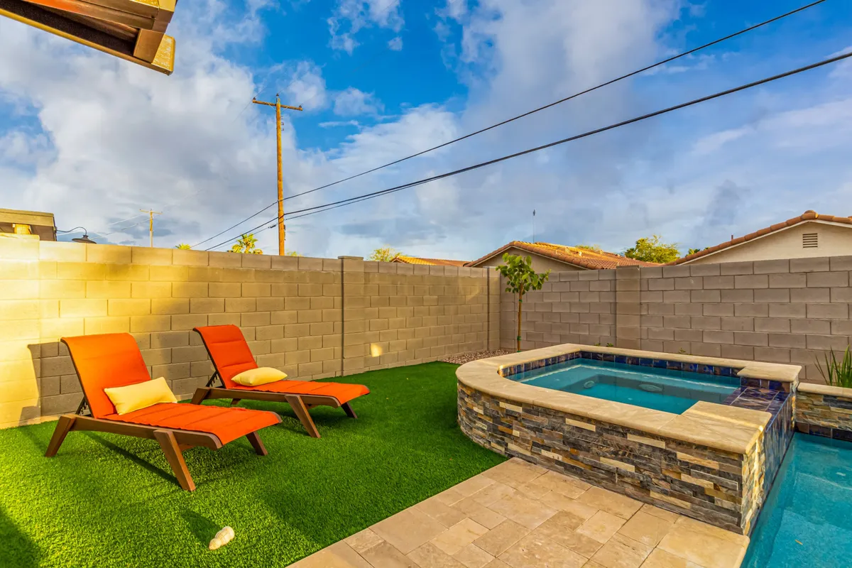 This image showcases an inviting outdoor spa area with orange lounge chairs arranged on green grass, a tranquil stone wall, and a sense of privacy ideal for unwinding. The setup hints at intimate conversations under the stars and relaxed, post-work gatherings.