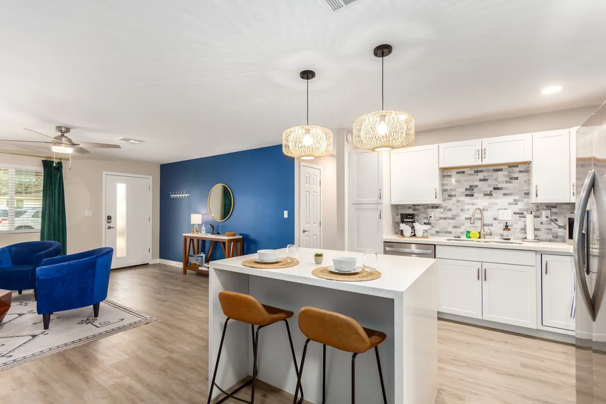A visually striking open-concept space featuring a blue accent wall, stylish modern light fixtures, a large kitchen island, and a comfortable seating area. The image captures the fluid connection between the kitchen and living spaces, with inviting decor and ample room for gathering.