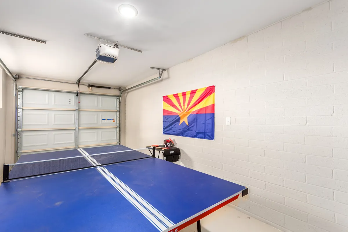 Another angle of the game room, this shot spotlights the ping pong table in front of the distinctive Arizona flag and provides a clear view of the garage-style door, suggesting a versatile and open space. The scene captures the welcoming vibe for gatherings and playful matches.
