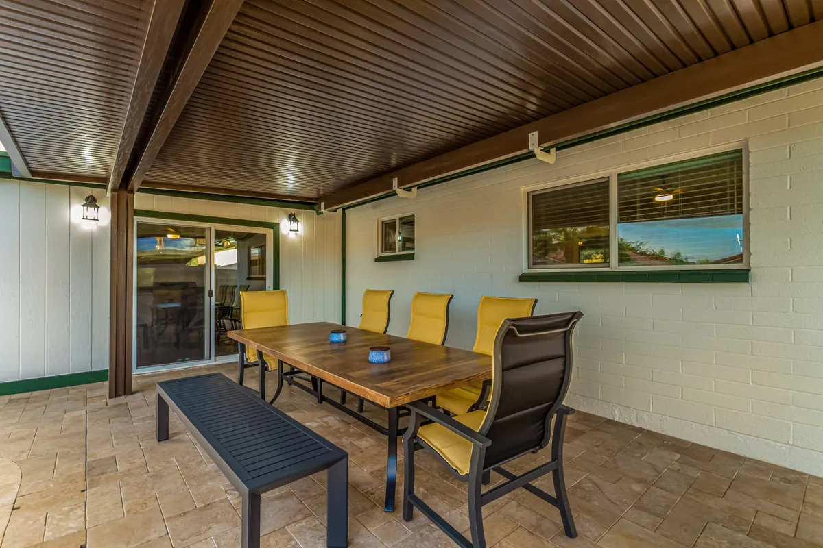 A cheerful dining room with a wooden table, vibrant yellow chairs, a black bench, and modern lighting fixtures. The setup is spacious enough for large dinner parties or intimate family breakfasts.