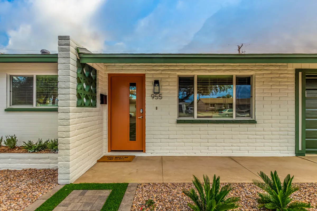 This image highlights the orange front door with green trim and the crisp white brick facade, offering a stylish and vibrant entrance. The inviting porch and spacious yard evoke a sense of arrival and opportunities to spend quiet moments outside.