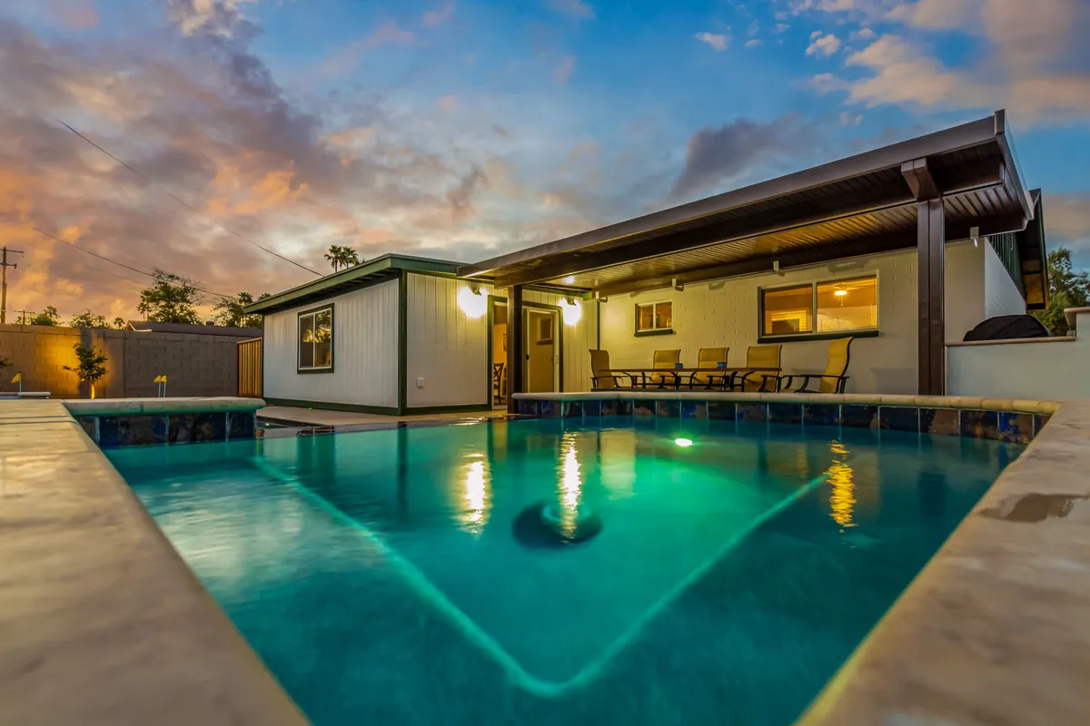 A tranquil backyard scene featuring a sparkling swimming pool, an inviting outdoor seating area, and the modern exterior of the home, all framed by twilight ambiance.