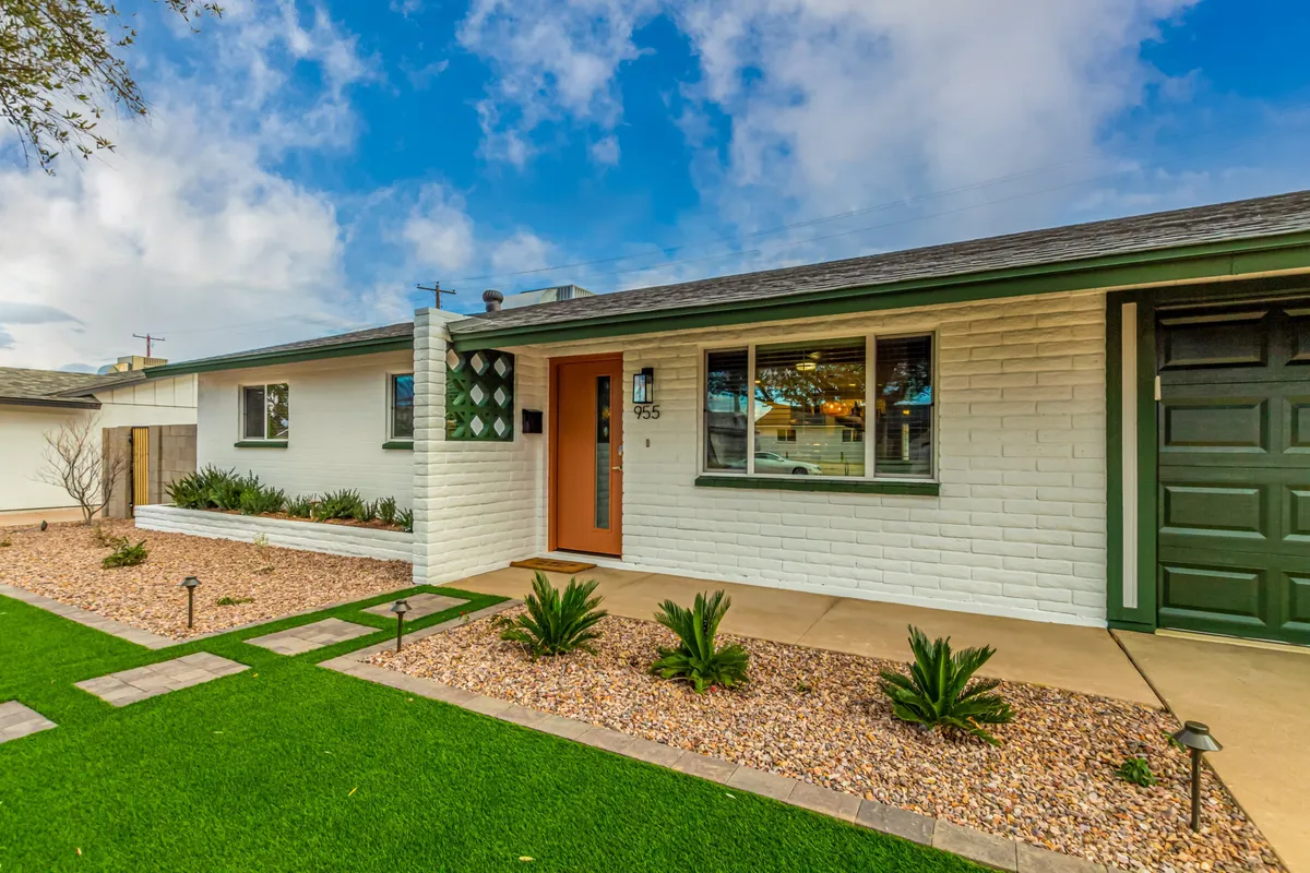 This exterior image features the front door with striking green accents, a neatly landscaped garden, and an airy, sunlit atmosphere. The setting feels lively and fresh, inviting guests to enjoy both the garden and outdoor living spaces.