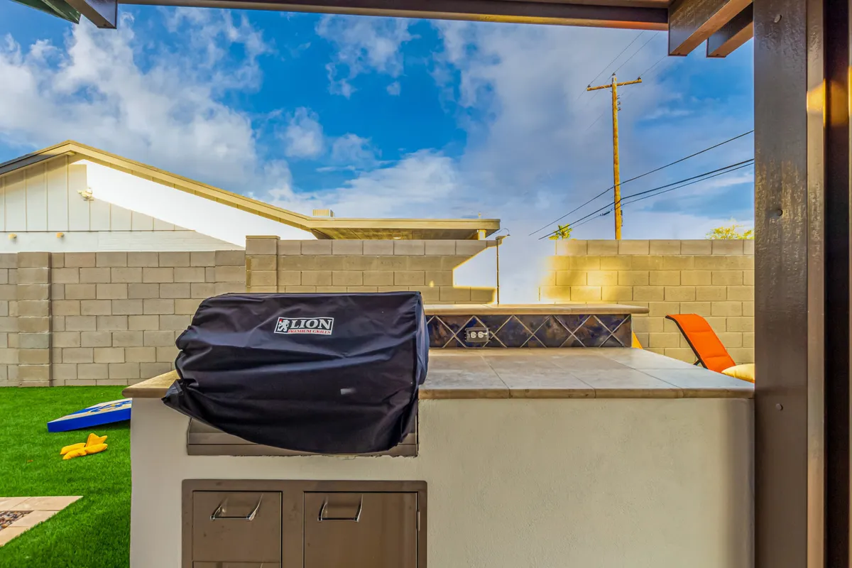 Here, the built-in BBQ grill, outdoor counter, and lounge chair are set beside landscaped lawns. The scene suggests al fresco cooking and dining, with ample space for guests to gather, relax, and enjoy outdoor meals against a backdrop of greenery.