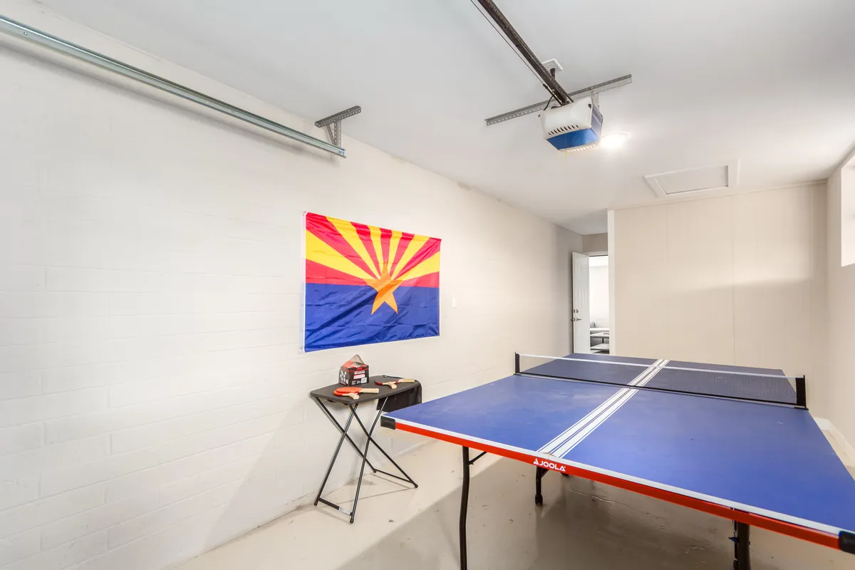This interior photo captures the heart of the game room, featuring a vibrant ping pong table as the centerpiece, an Arizona flag adding a local touch, and a small table with various items. The space is clearly set up for active play and group gatherings, exuding a lively and fun environment ideal for families and friends.