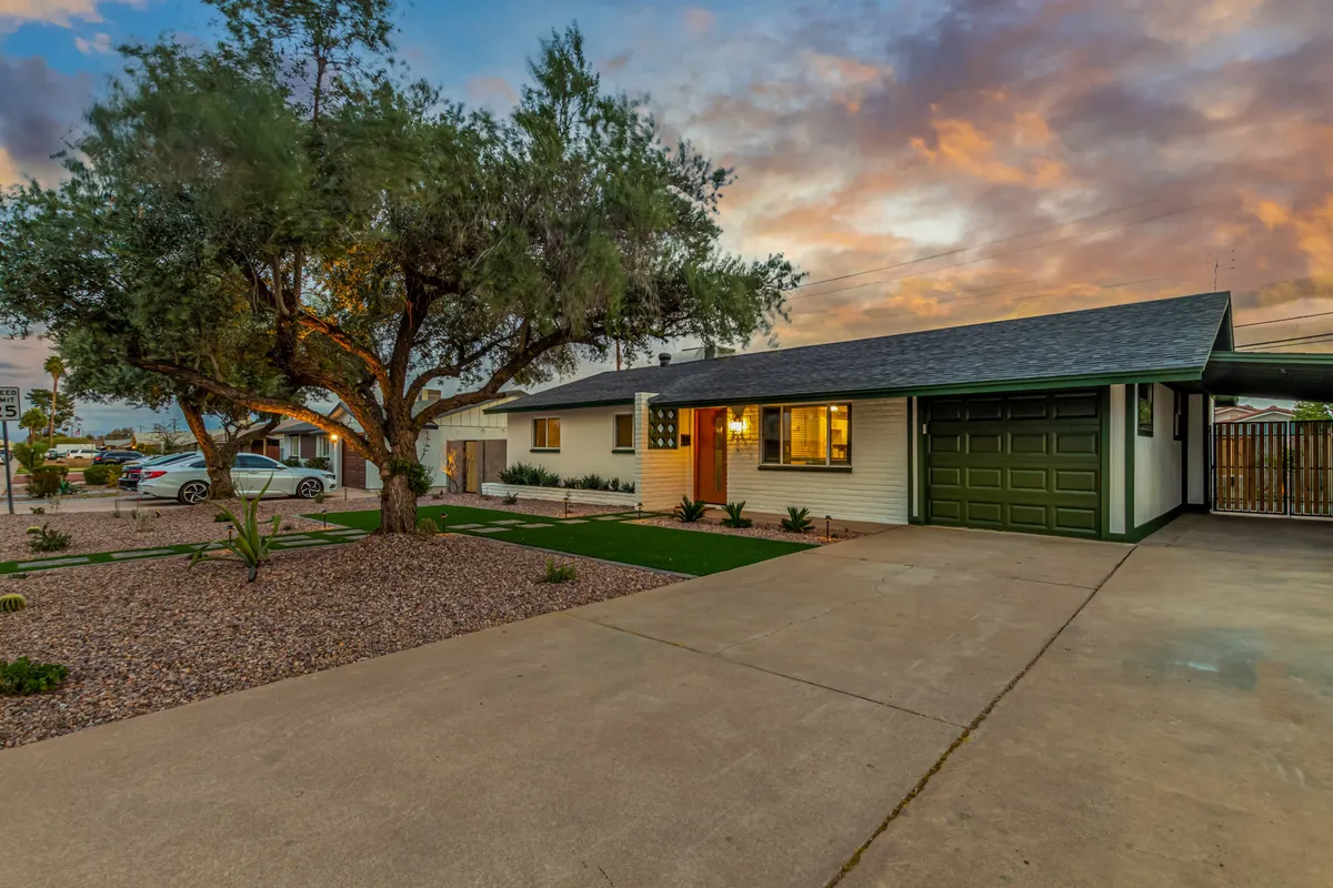 This image showcases the exterior of the property, with a large tree in the front yard, a well-lit entrance, and a welcoming garage door. The inviting atmosphere is accentuated by sunset lighting, and the open front yard connects naturally to the outdoors.
