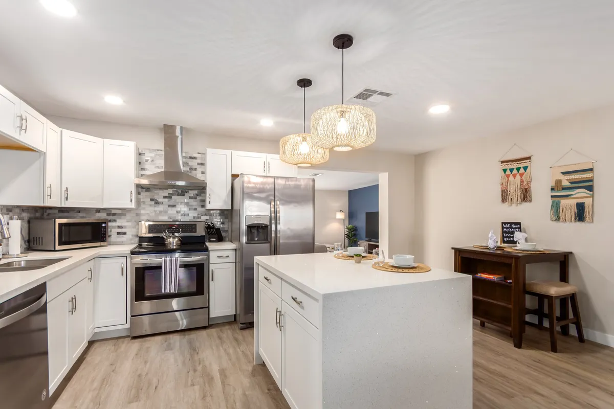 A close-up of a contemporary kitchen with a prominent island countertop, pendant lighting, stainless steel appliances, and elegant backsplash tile. The setup is ideal for preparing meals, casual dining, or hosting game nights.