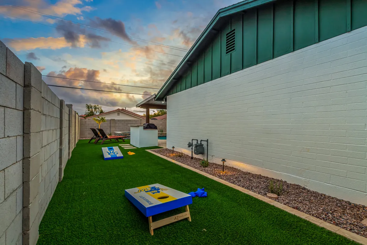 The backyard comes alive with playful energy—cornhole boards on a green lawn, relaxed seating, and the inviting house facade set under sunset light. Guests enjoy games and social gatherings, illustrating the blend of fun and comfort the space offers.