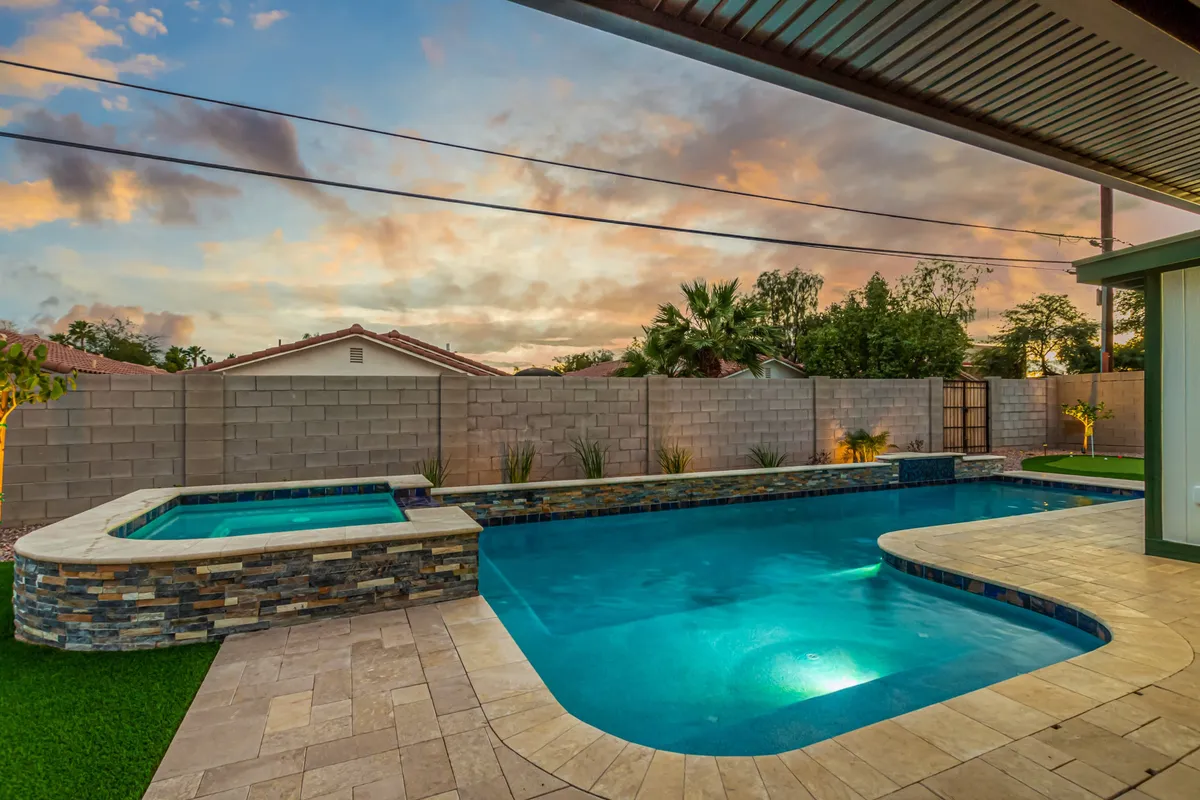 This image displays the heart of the outdoor oasis: a shimmering swimming pool, bubbling spa, lush landscaping, and expansive sky. Stylish lounge seating surrounds the pool, while palm trees and manicured greenery frame the serene setting, evoking a luxurious resort ambiance.