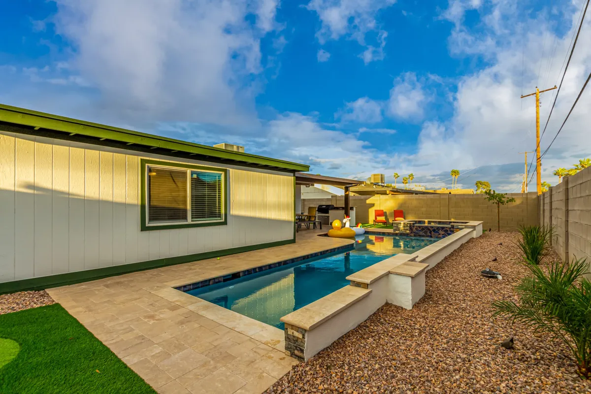 A vibrant exterior shot featuring the swimming pool, outdoor seating, a landscaped garden, and the house facade, all bathed in natural light. The space evokes leisure and togetherness.