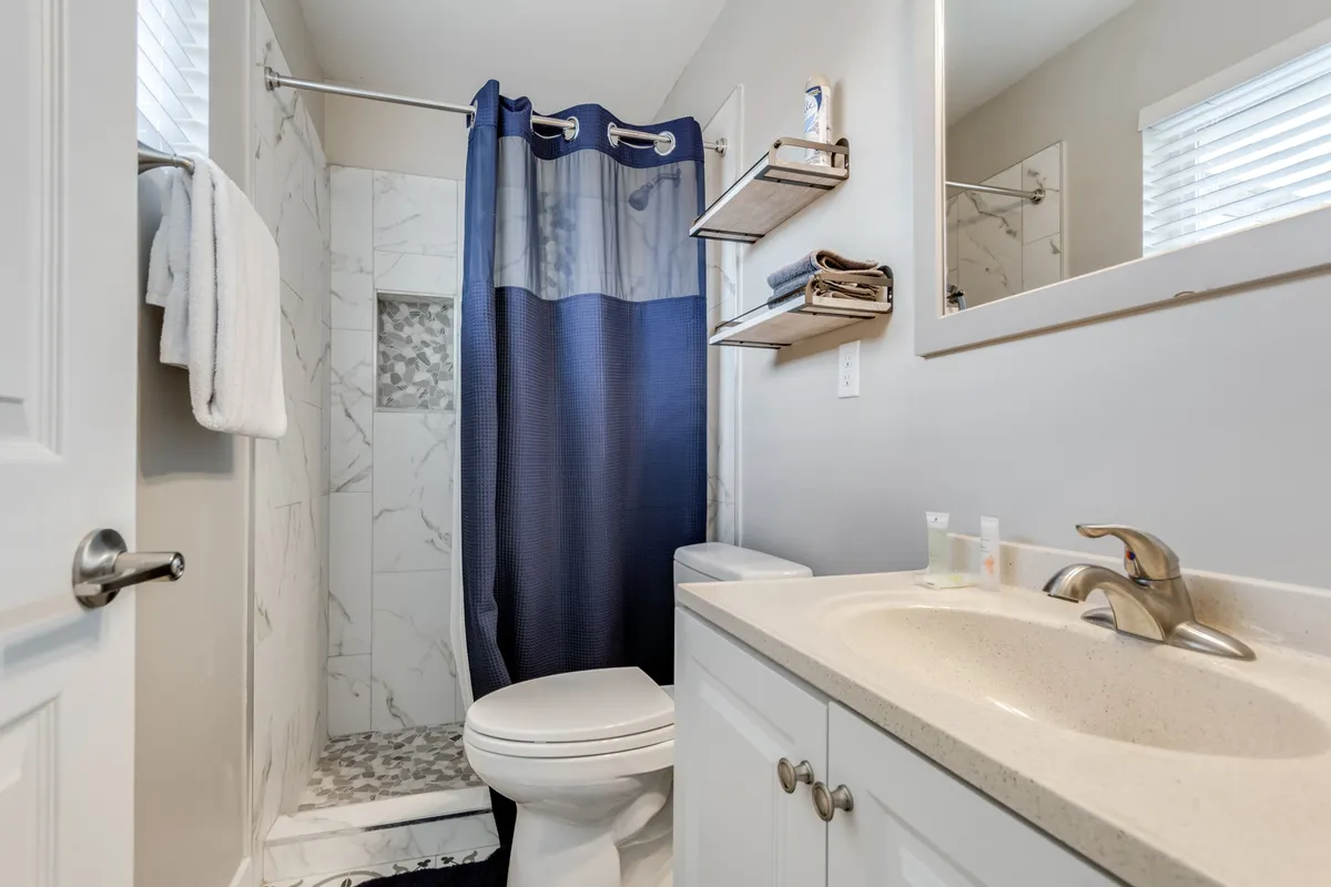 A modern, inviting bathroom showcasing a spacious shower area, a sleek sink, and a large mirror. The neutral palette and clean lines suggest recent renovations, offering a spa-like atmosphere for personal care routines.