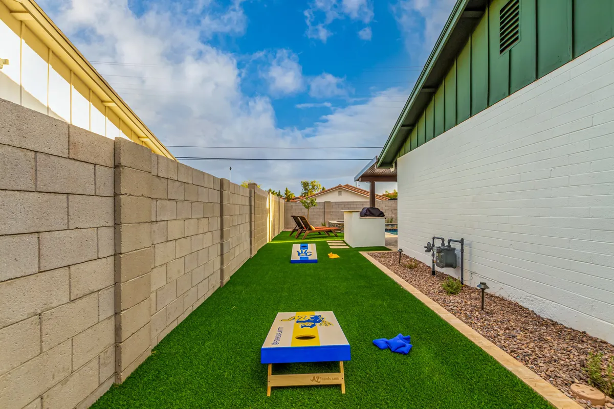 A playful backyard setup with a green lawn hosting cornhole boards, lounge chairs perfect for relaxing, and a grill area, creating an inviting spot for family games and gatherings.