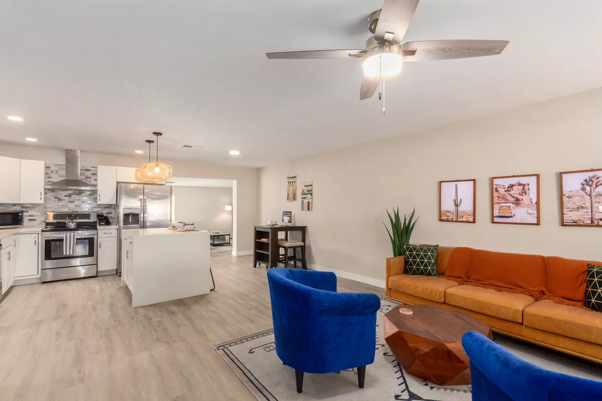 A warm, inviting interior view with blue chairs, an orange couch, a kitchen island, and decorative wall art. The layout encourages group interaction—ideal for socializing, cooking together, and relaxing in comfort.