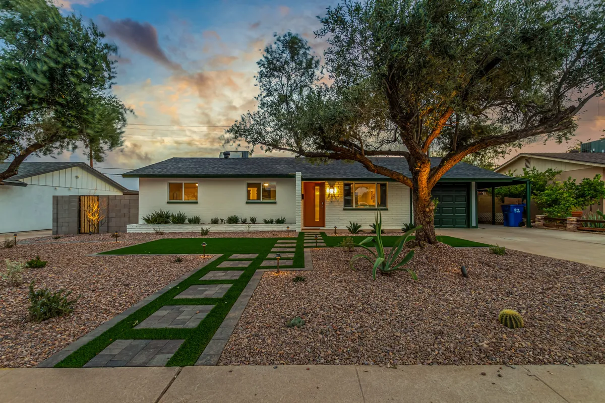 The image captures the front exterior of the home, with a landscaped pathway leading to the front door under the shade of a large tree. The setting is welcoming, professional, and ideal for first impressions or gathering the team before heading out to explore the neighborhood.